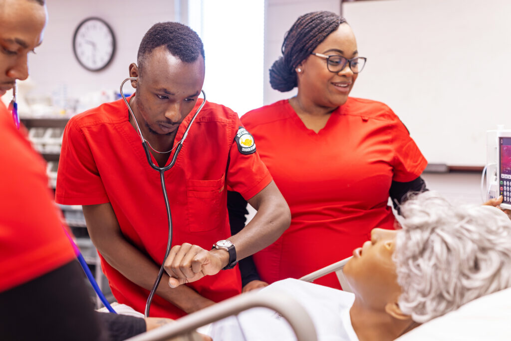 Three nursing students practice checking blood pressure on a medical manikin